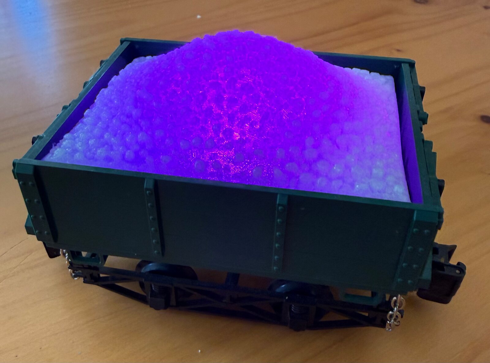 3D-printed coal load in semi-translucent glow filament, lit purple from underneath by an LED, in a green G scale side dump ore car