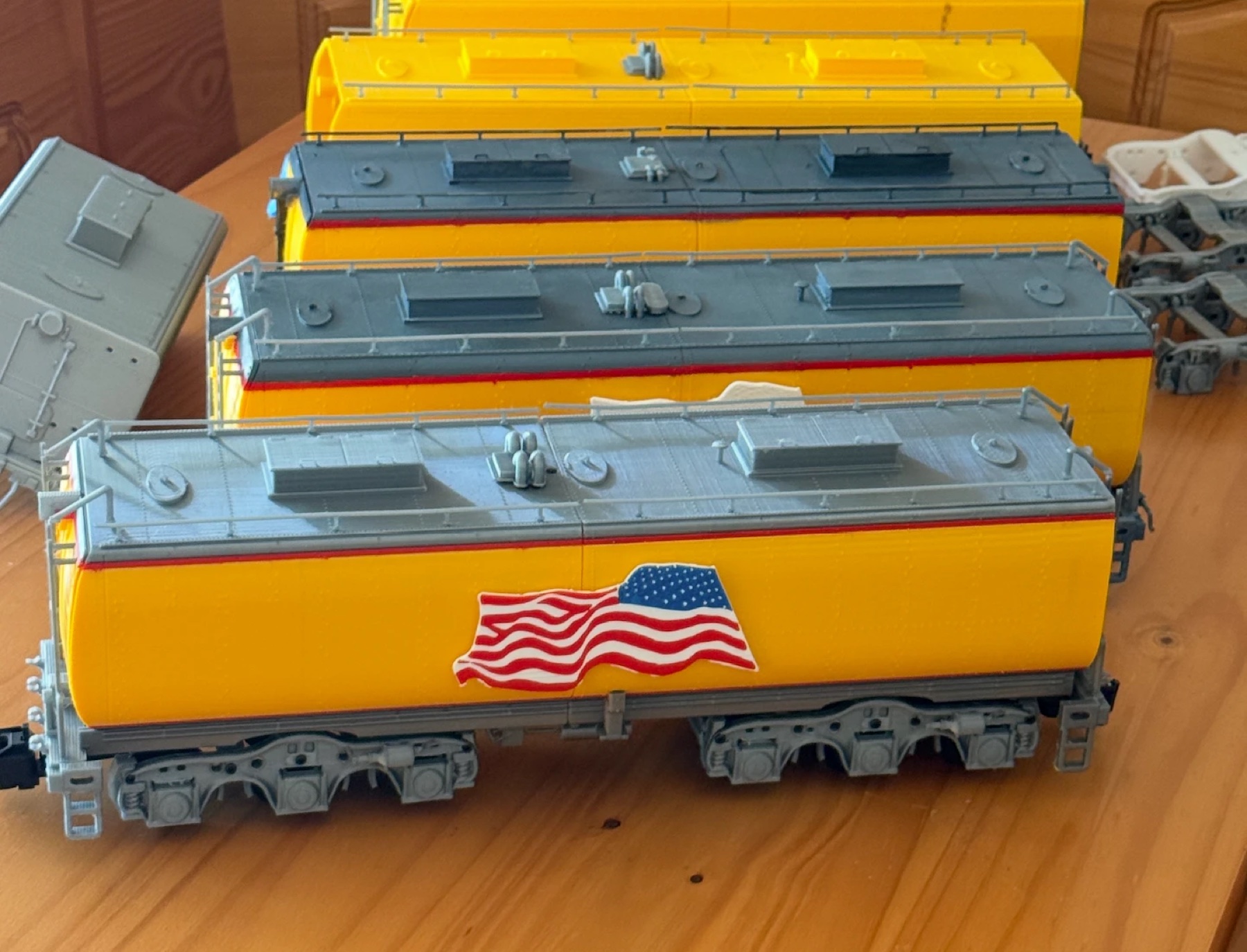 3D-printed G scale auxiliary water tender, car 809, in yellow and gray with red stripes and a flag plaque, with earlier test prints behind it