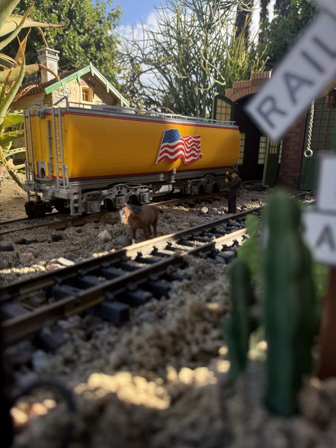 3D-printed G scale auxiliary water tender, car 809, on garden railroad track in front of a brick engine house, with a figure and a horse beside the rails